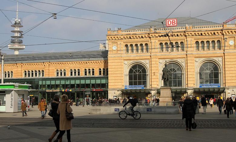 Bahnhof Berlin mit DB-Logo, Fahrgäste und Fahrradfahrer vor historischem Gebäude, Busbahnhof und urbane Atmosphäre, zentrale Verkehrsverbindung, Reise und Mobilität in Deutschland.